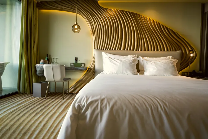 Zimmer mit weißem Bett vor hohem Kopfteil aus Holz