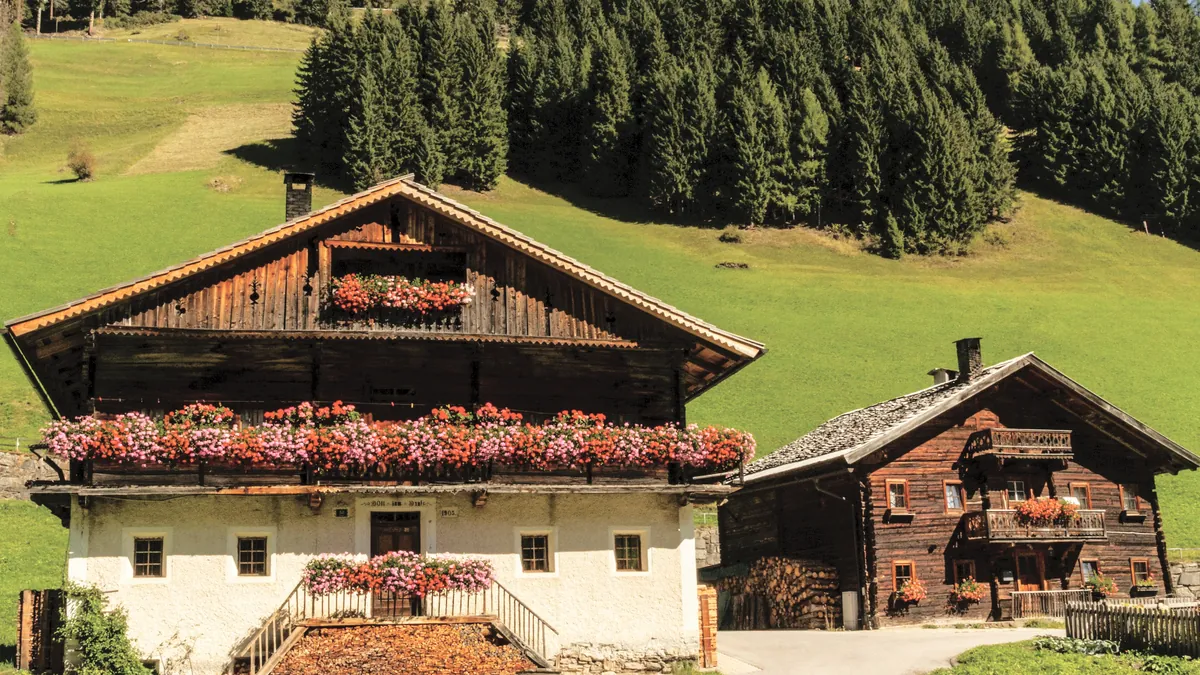 Tiroler Bauernhaus mit Blumenbalkonen vor grünen Wiesen